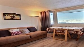 Een gezellige kamer met een bank, een klein tafeltje en uitzicht op bergen door een raam.