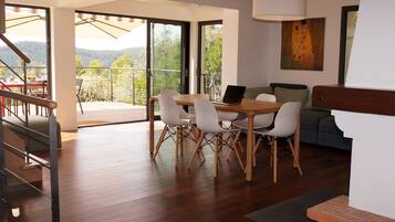 Un salon moderne avec une table à manger en bois, des chaises blanches et un canapé. Il y a un balcon avec vue sur l’extérieur.