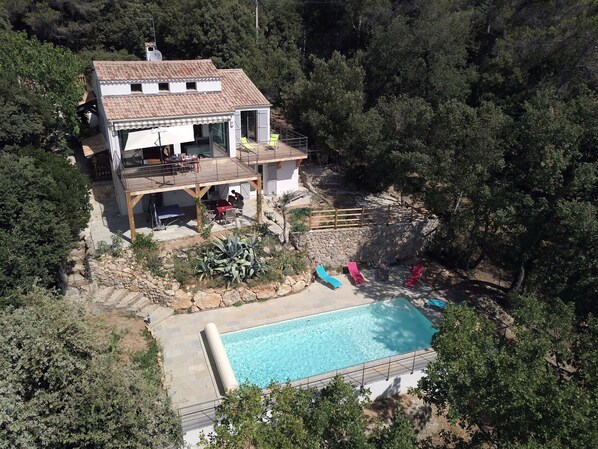 A two-story house with a swimming pool, outdoor seating, and a stone wall.