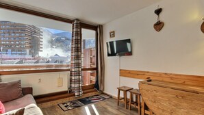 A cozy room with a wooden bench, a TV mounted on the wall, and a view of a snowy mountain and buildings. - Renovated studio 3 pers, south-facing with balcony in La Plagne (La Plagne)