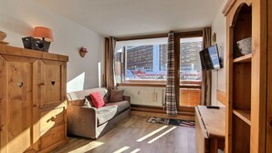 A cozy room with a sofa, wooden cabinet, and a TV mounted on the wall. - Renovated studio 3 pers, south-facing with balcony in La Plagne (La Plagne)