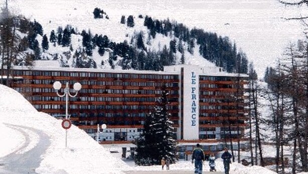 Un bâtiment sur lequel on peut lire l’inscription « LE FRANCE », avec une montagne enneigée en arrière-plan.