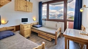 Une chambre avec un lit, un bureau et une vue sur les montagnes, visible à travers de grandes fenêtres.
