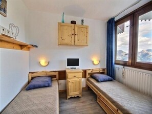 Une petite pièce agréable, dotée de deux lits en bois, d’un bureau avec un ordinateur et d’une fenêtre donnant sur les montagnes.