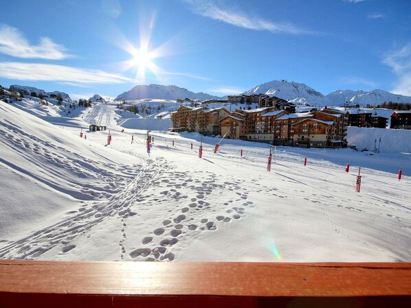 Pista de esquí cubierta de nieve con huellas, una valla de madera y una hilera de edificios de madera con nieve en los tejados.