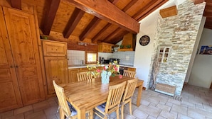 A wooden dining table with six chairs, a vase with flowers, and a kitchen in the background.