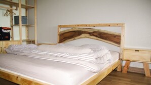 A wooden bed with a unique headboard design, a bedside table, and a wooden wardrobe in a room with a wooden floor.