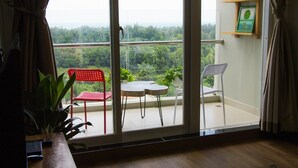 A balcony with a table and two chairs, a potted plant, and a view of a forested area.
