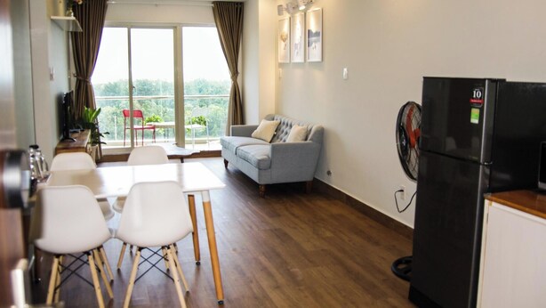 A modern living room with a grey sofa, white chairs, a dining table, and a black refrigerator.