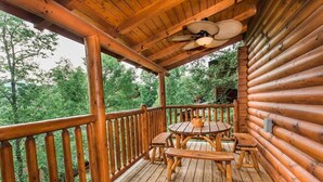A wooden deck with a table and benches, surrounded by a wooden railing, overlooking a forested area.