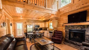 A log cabin interior with a living room, dining area, kitchen, and fireplace.