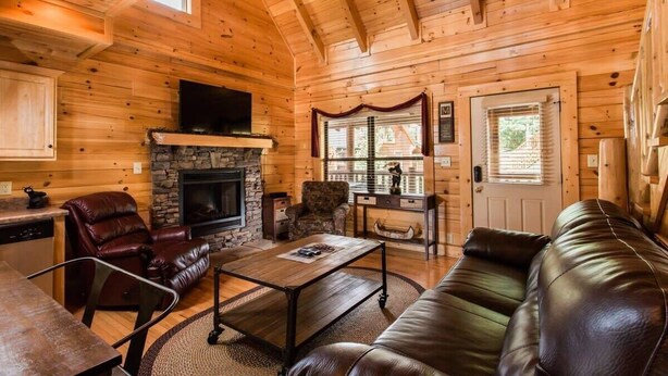 A cozy log cabin interior with a fireplace, leather furniture, and a stone accent wall.