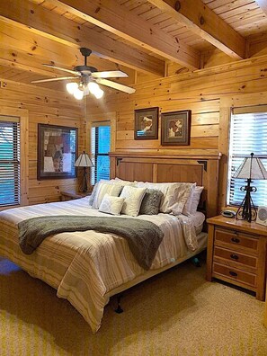 A wooden cabin bedroom with a bed, nightstands, a ceiling fan, and framed pictures on the walls. - 10 Min 2 Pigeon Forge Pkwy/Gorgeous Cabin/Hot Tub (Pigeon Forge)