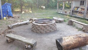 A rustic outdoor area with a fire pit, wooden benches, and a small wooden structure. - Hideout in the Woods (Au Sable Charter Twp)