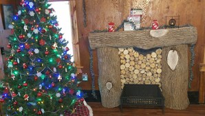 A Christmas tree with lights and ornaments, a fireplace with logs, and a plaid rug. - Hideout in the Woods (Au Sable Charter Twp)