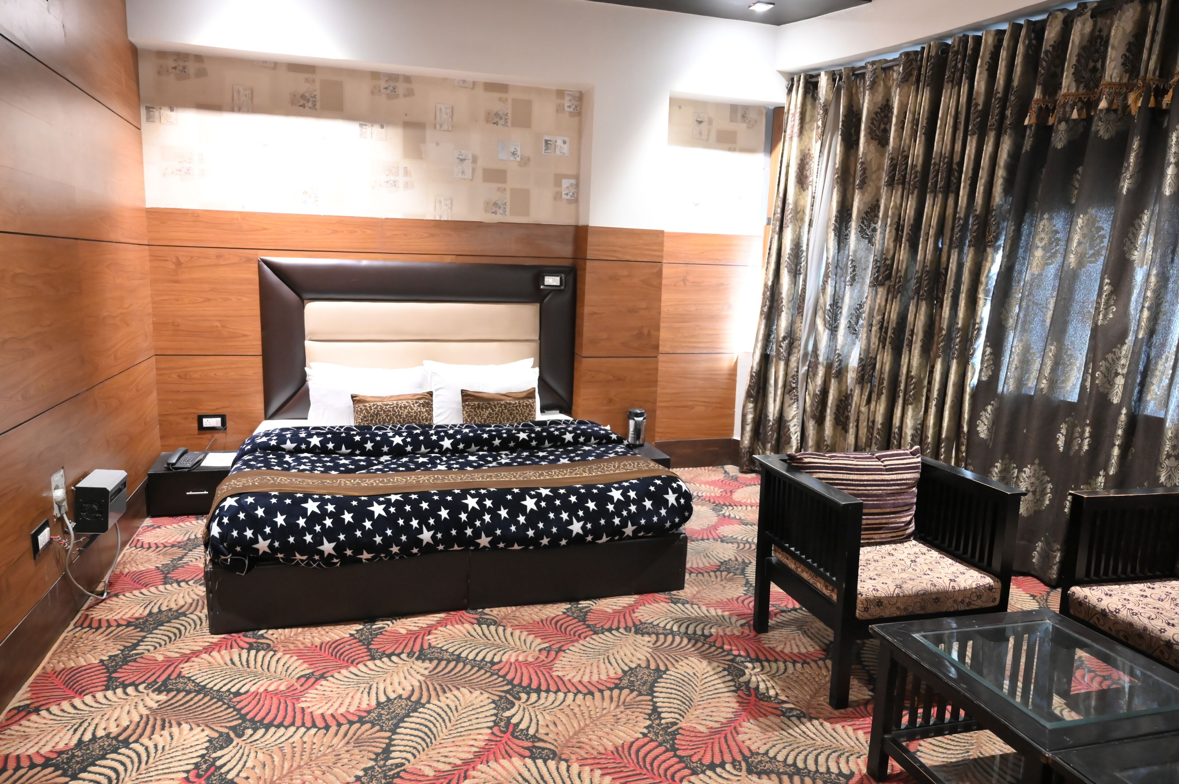 A hotel room with a large bed, a glass coffee table, and a seating area with two chairs.
