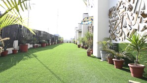 Un sendero con césped artificial, plantas en macetas y una pared con diseño de mosaico.