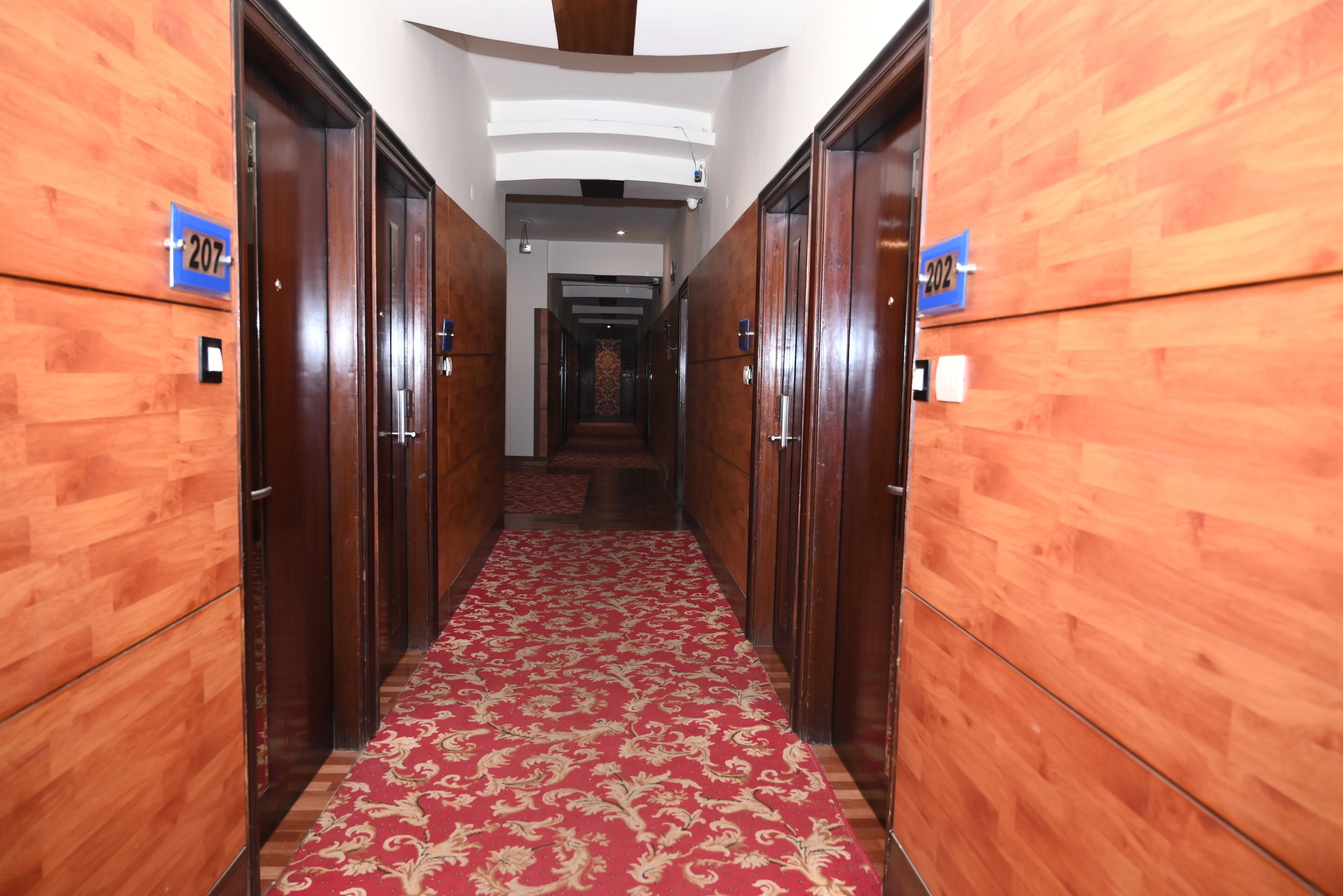 A corridor with wooden walls and a red carpet, leading to a room with a number sign.