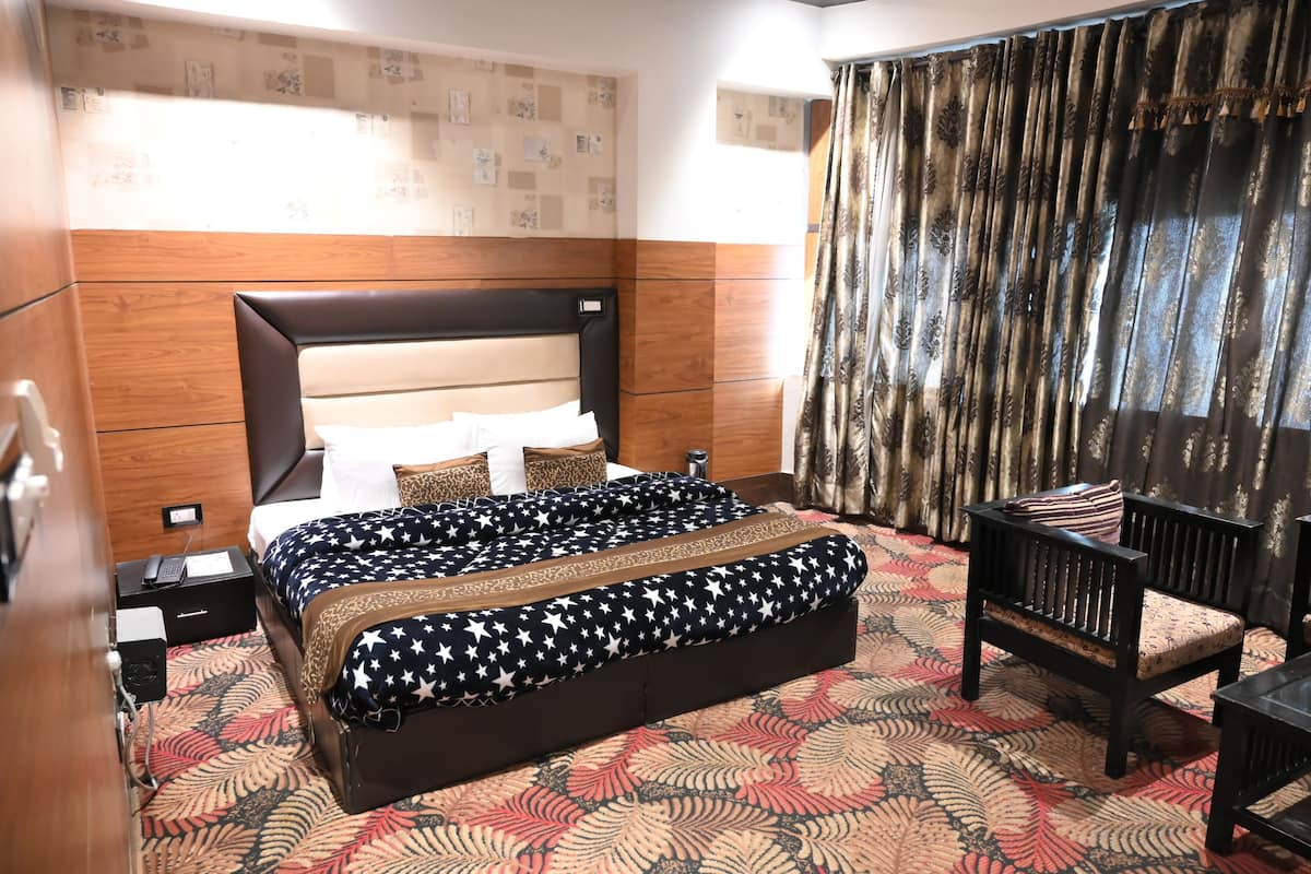 A hotel room with a large bed, a wooden headboard, a patterned carpet, and a dark curtain.