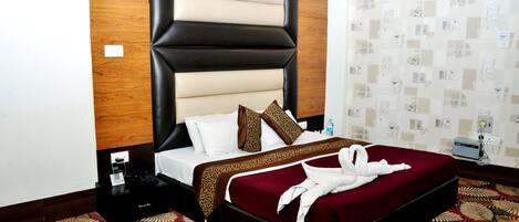 A hotel room with a large bed, a wooden headboard, a patterned carpet, and a wall with a floral wallpaper design.