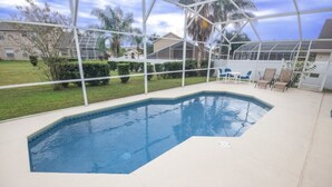 Une piscine entourée d’une enceinte en verre, avec une pelouse et des chaises tout autour.