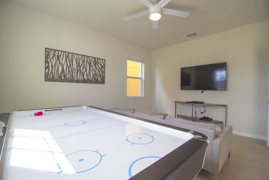 A room with a pool table, a ceiling fan, a television, and a window.