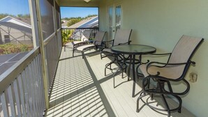 Een overdekt buitengebied met een tafel, stoelen, een plafondventilator en een uitzicht op huizen op de achtergrond.