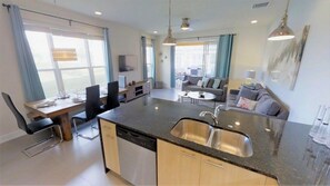 A modern kitchen with a central island, built-in dishwasher, and a dining area with a table and chairs. - Aco235895 - The Retreat at Champions Gate - 3 Bed 3 Baths Townhome (Clermont)
