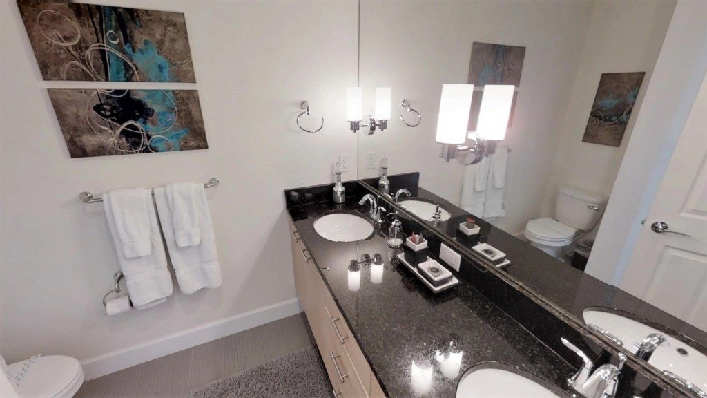 A modern bathroom with two sinks, a large mirror, and artwork on the walls.