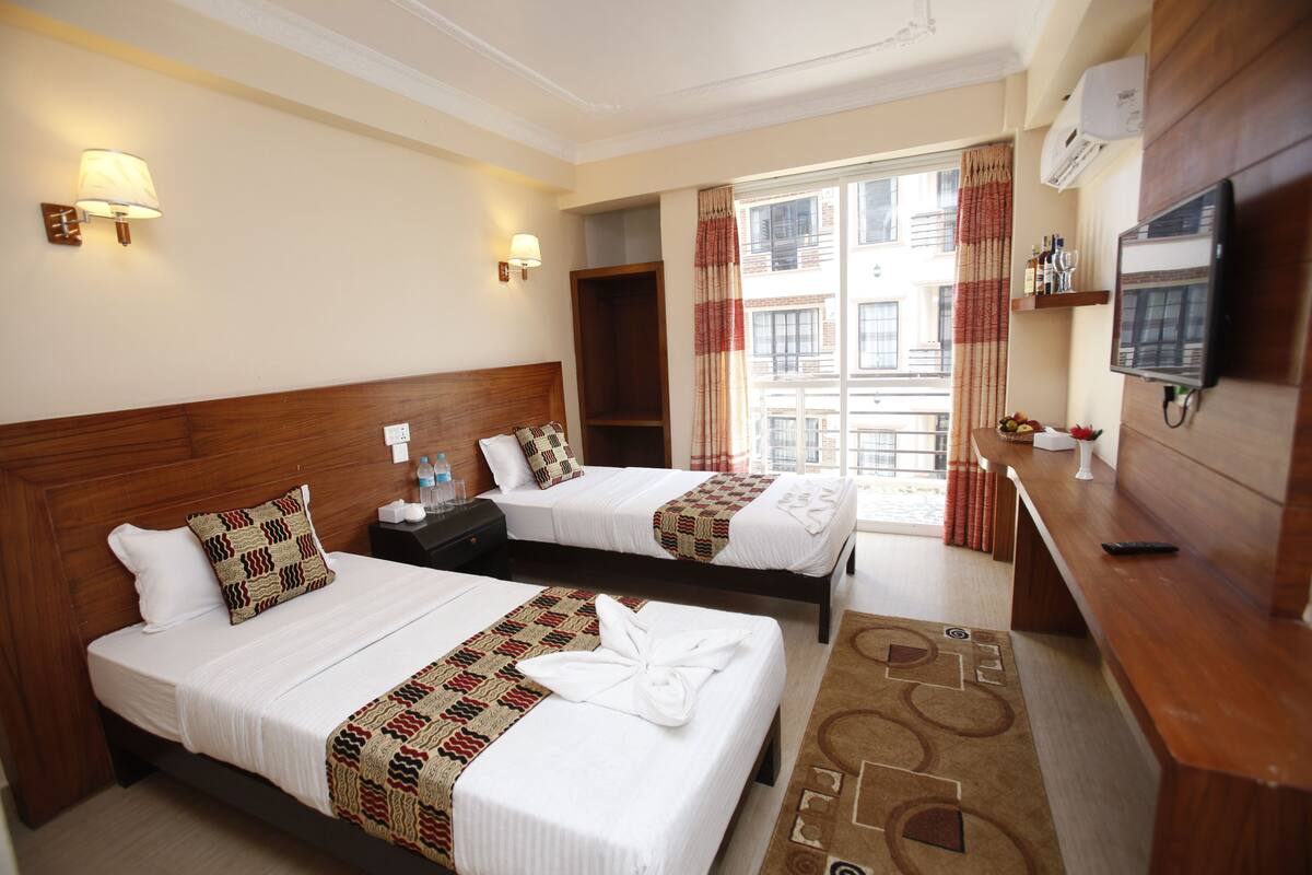 Une chambre d’hôtel avec deux lits, une télévision, un bureau et une fenêtre avec des rideaux.