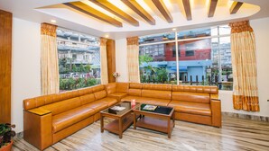 A modern living room with a large sectional sofa, two coffee tables, and large windows with curtains. - Durbar Suite (Pokhara)