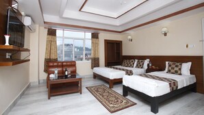 A hotel room with two beds, a sofa, a coffee table, a TV, and a window with curtains. - Durbar Suite (Pokhara)