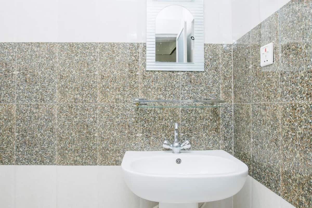 Une salle de bain avec un lavabo blanc, une étagère en verre au-dessus et un miroir au-dessus de l’étagère. Les murs sont recouverts de carreaux à motifs pointillés.