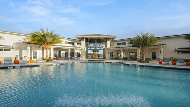 A swimming pool with lounge chairs and palm trees, surrounded by buildings with large windows and a covered area. - Aco237972 - Sonoma Resort - 6 Bed 4 Baths Villa (Kissimmee)