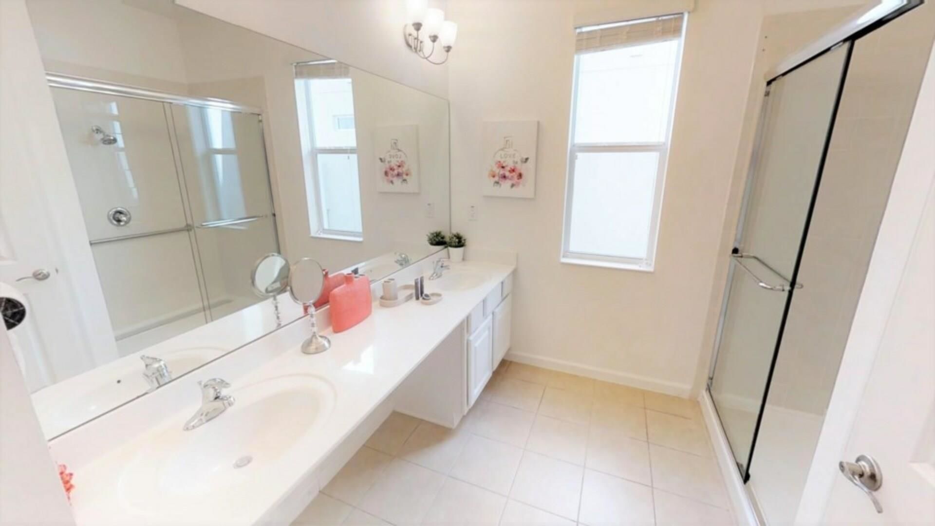 A modern bathroom with a large mirror, two sinks, a shower, and a glass-enclosed shower area.