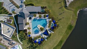 An aerial view of a resort with a central swimming pool, multiple lounge areas with umbrellas, and a body of water adjacent to the property. - Aco237972 - Sonoma Resort - 6 Bed 4 Baths Villa (Kissimmee)