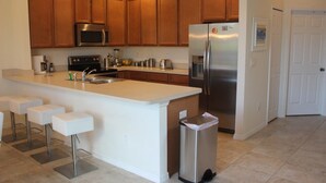 A kitchen with wooden cabinets, stainless steel appliances, a central island with bar stools, and a trash bin. - Aco106374 - Bella Vida Resort - 4 Bed 3 Baths Townhouse (Kissimmee)