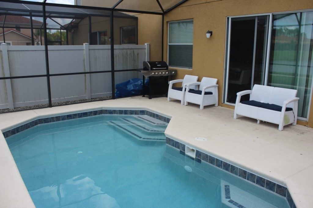 A swimming pool with a hot tub, a grill, and two white chairs.
