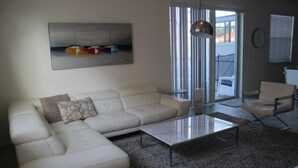 A living room with a white sectional sofa, a glass coffee table, and a gray carpet. There is a painting of boats on the wall and a window with blinds. - Aco106374 - Bella Vida Resort - 4 Bed 3 Baths Townhouse (Kissimmee)