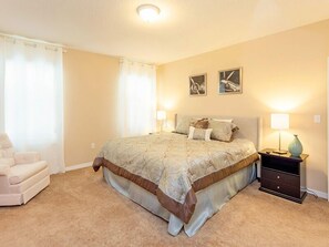 A bedroom with a large bed, two bedside lamps, a nightstand, a chair, and two wall art pieces. - Fv49464 - Cypress Pointe - 5 Bed 4.5 Baths Villa (Davenport)
