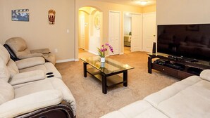 A living room with a sofa, a glass coffee table, a TV, and a hallway leading to another room. - Fv49464 - Cypress Pointe - 5 Bed 4.5 Baths Villa (Davenport)