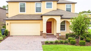 A two-story house with a garage, a red door, and a brick driveway. - Fv49464 - Cypress Pointe - 5 Bed 4.5 Baths Villa (Davenport)