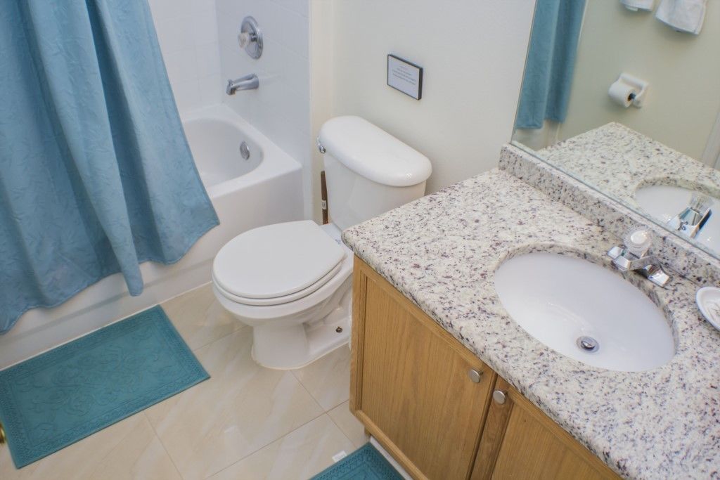 A bathroom with a white toilet, a bathtub, a sink with a granite countertop, and a blue shower curtain.