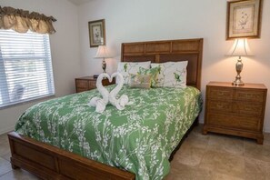 A neatly made bed with a floral bedspread, two wall-mounted lamps, a wooden nightstand, and a framed picture on the wall. - Ip60473 - Southern Dunes - 3 Bed 2 Baths Villa (Haines City)