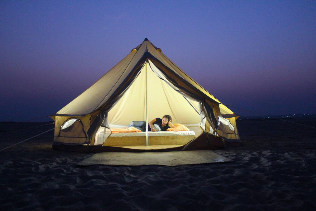 A tent with a bed inside, set up on a sandy surface.