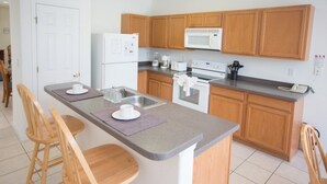 A modern kitchen with wooden cabinets, a granite countertop, a built-in oven, a microwave, and a refrigerator. There are two wooden chairs at the kitchen island.