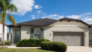 A single-story house with a front garage, a small front yard with a palm tree, and a clear blue sky.