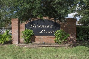 Een bord voor Sunrise Lakes, met een bakstenen bogenpoort en begroeiing eromheen.