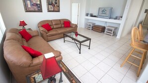 A living room with a brown sofa, red cushions, a glass coffee table, and a TV on a white stand.