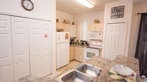 A kitchen with white cabinets, a stainless steel sink, a microwave, and a clock on the wall. - Ip60382 - Fiesta Key - 4 Bed 3.5 Baths Townhome (Kissimmee)